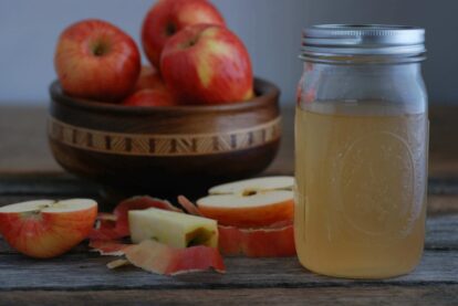 Fresh apples and homemade apple cider vinegar in a jar on a rustic table.