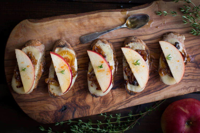 Apple bruschetta with caramelized apples and fresh herbs on wooden serving board.