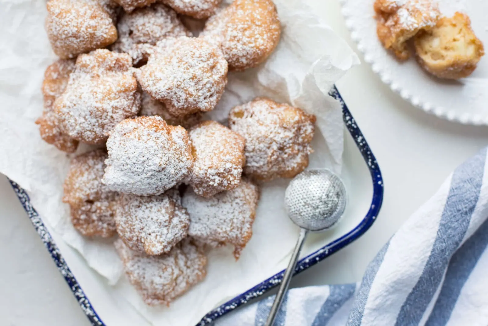 Fresh apple fritters dusted with powdered sugar on a white tray.