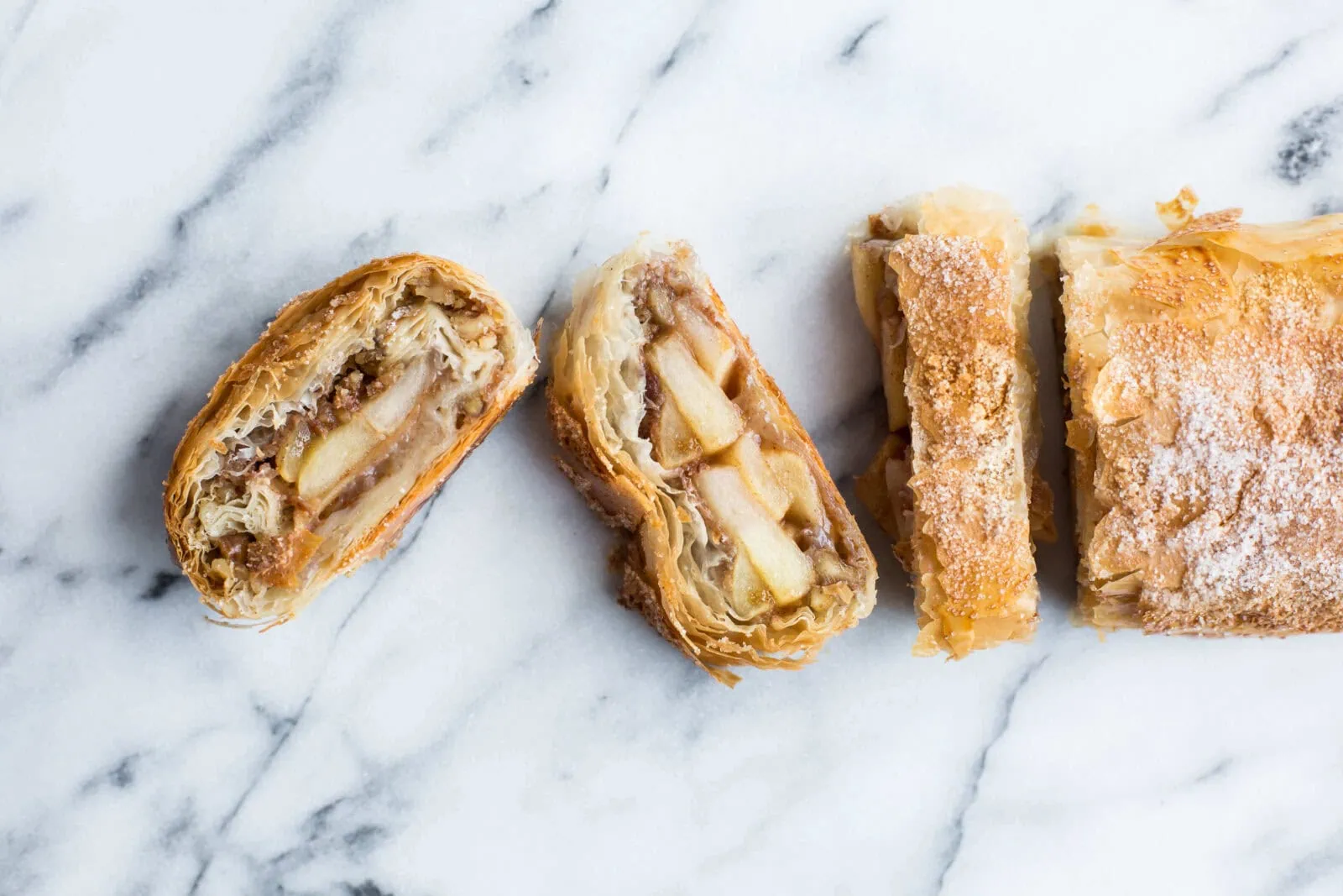 Apple strudel with phyllo dough and apple filling on marble surface.