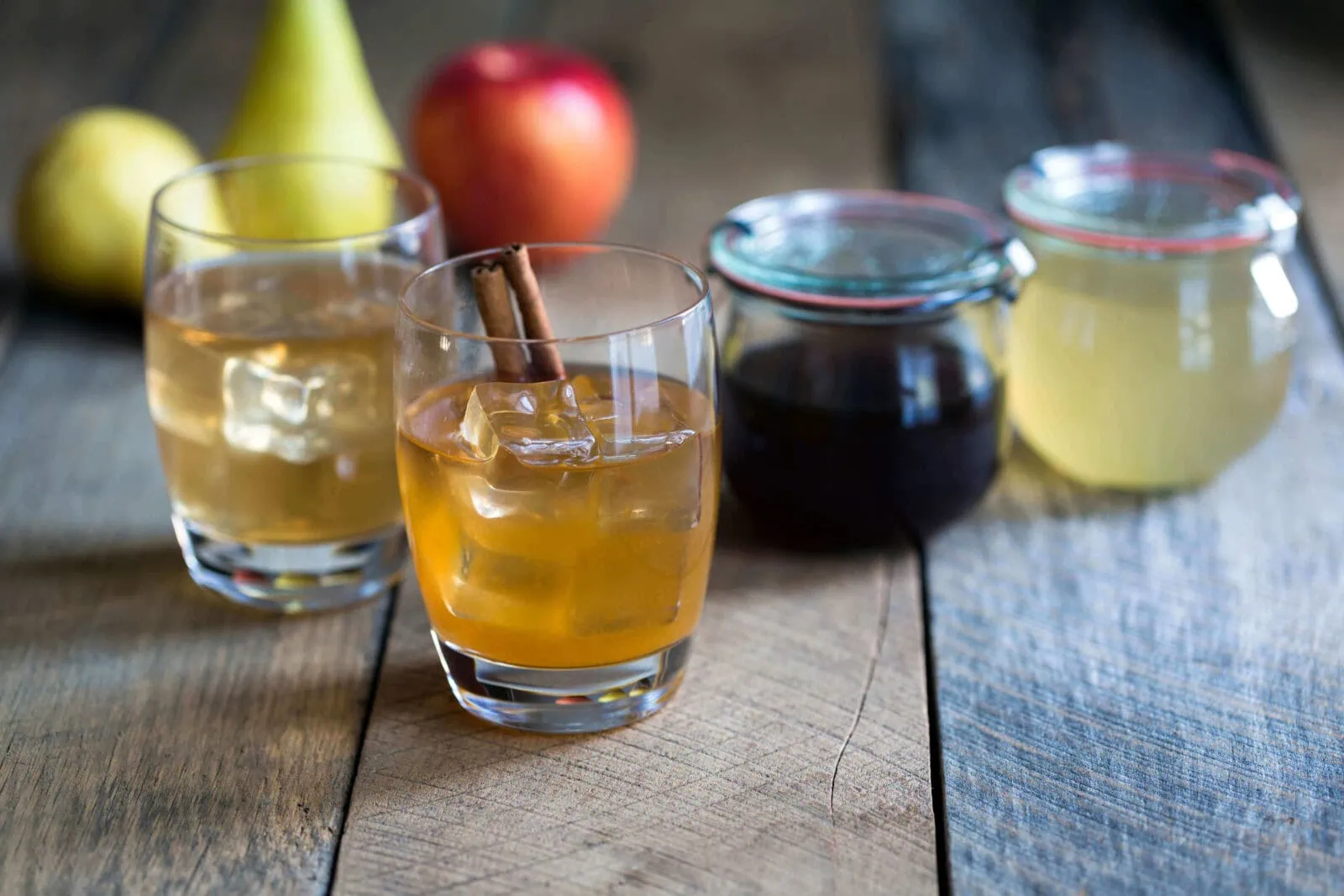 Citrus pear cocktail with cinnamon stick and fresh fruit on wooden table.
