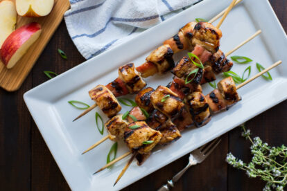 Maple soy grilled chicken and apple skewers on a white plate with green garnish.