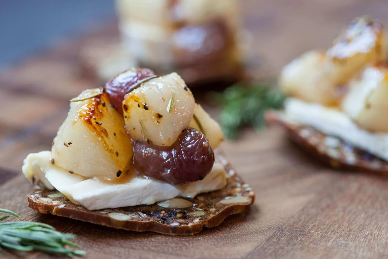 Roasted pear and red grape compote on a cracker with herbs and cheese.