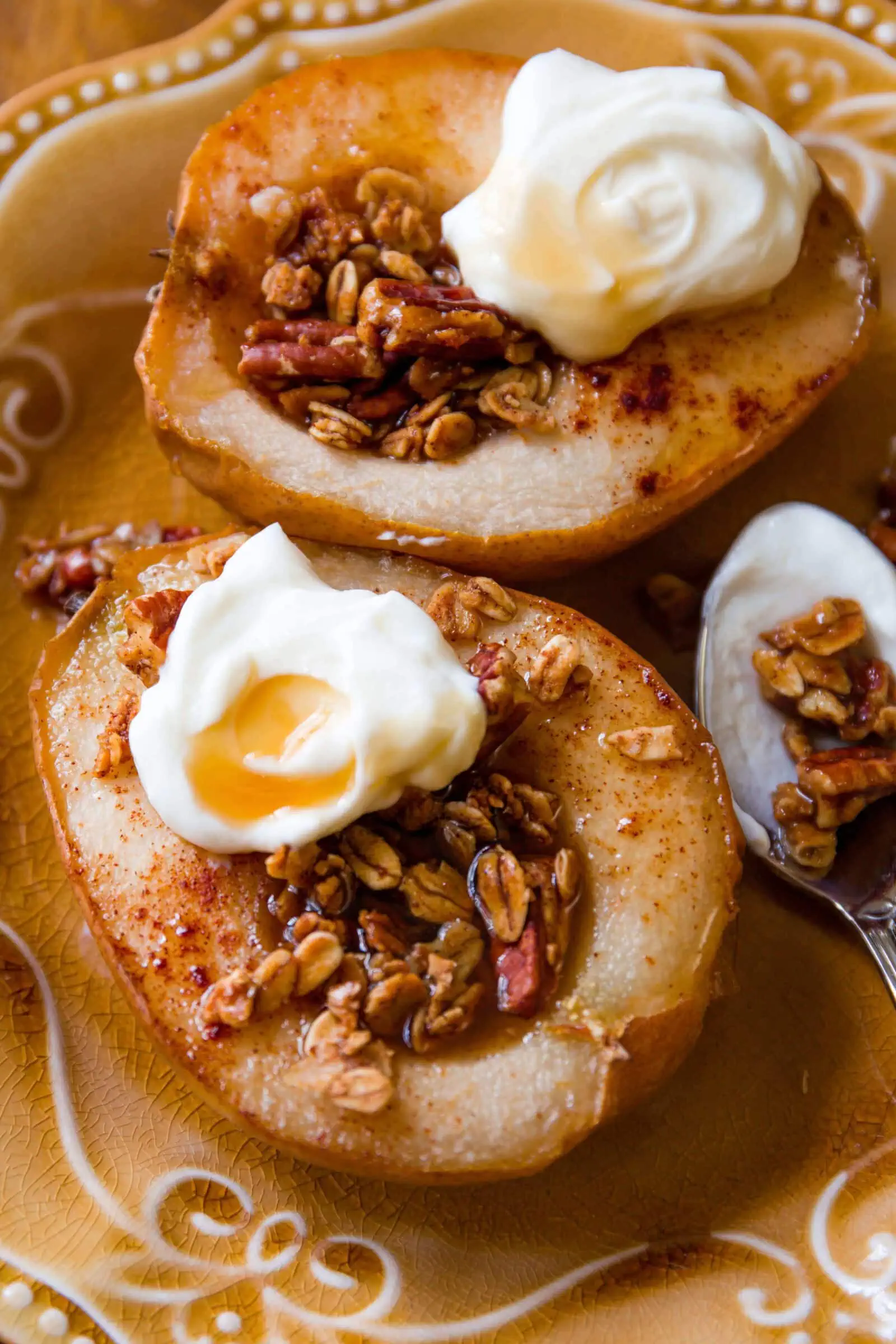 Baked pears topped with whipped cream and granola on a decorative plate.
