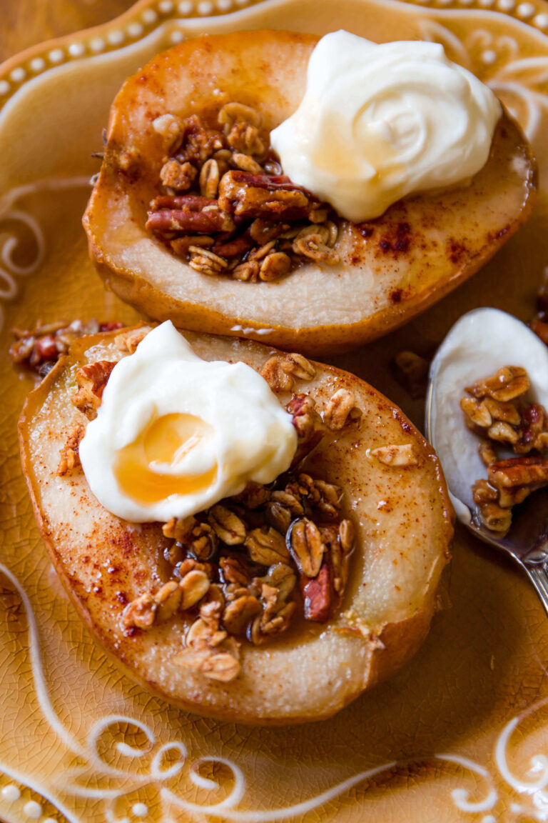 Baked pears topped with whipped cream and granola on a decorative plate.
