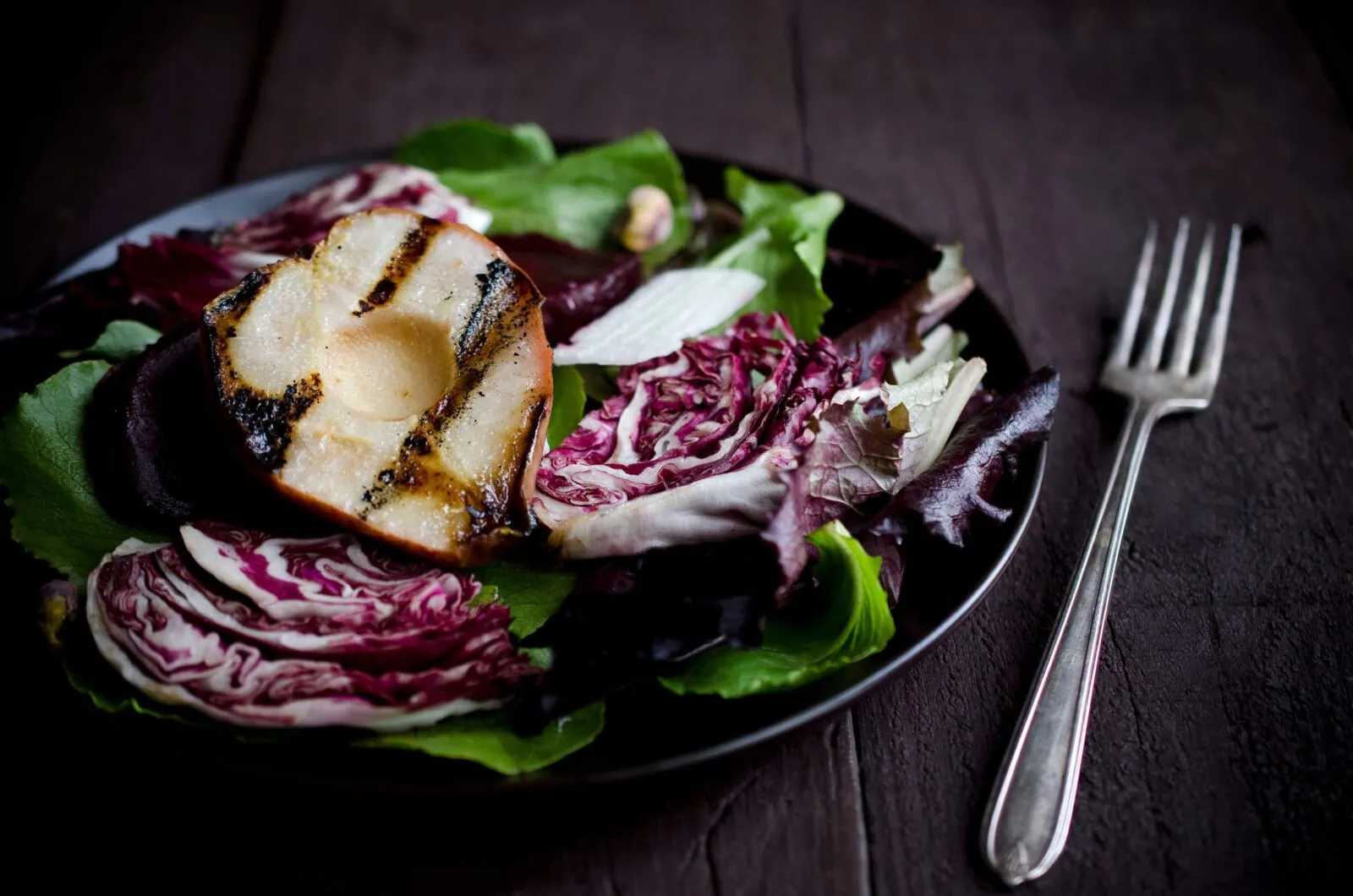 Grilled pear and radicchio salad with mixed greens on a black plate.