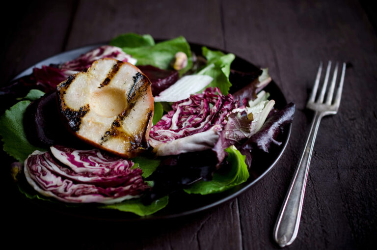 Grilled pear and radicchio salad with mixed greens on a black plate.