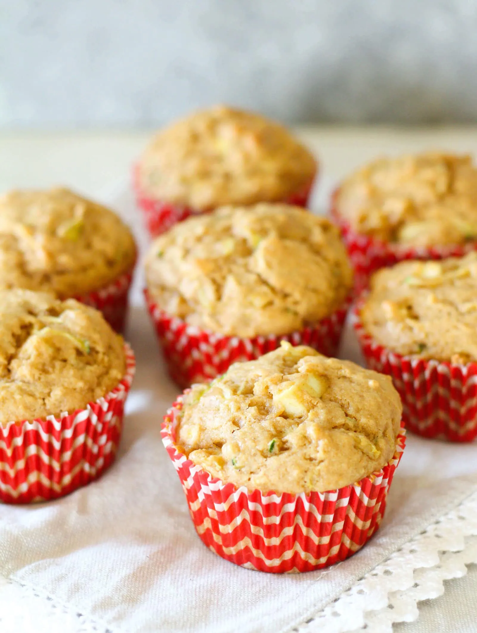 Fresh apple zucchini muffins in red and white paper cups on a white cloth.