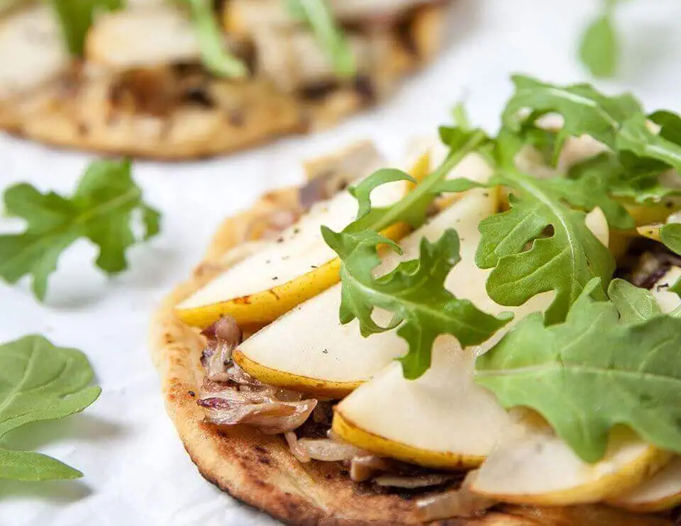 Pear pizzette topped with arugula and cheese on a crispy crust.
