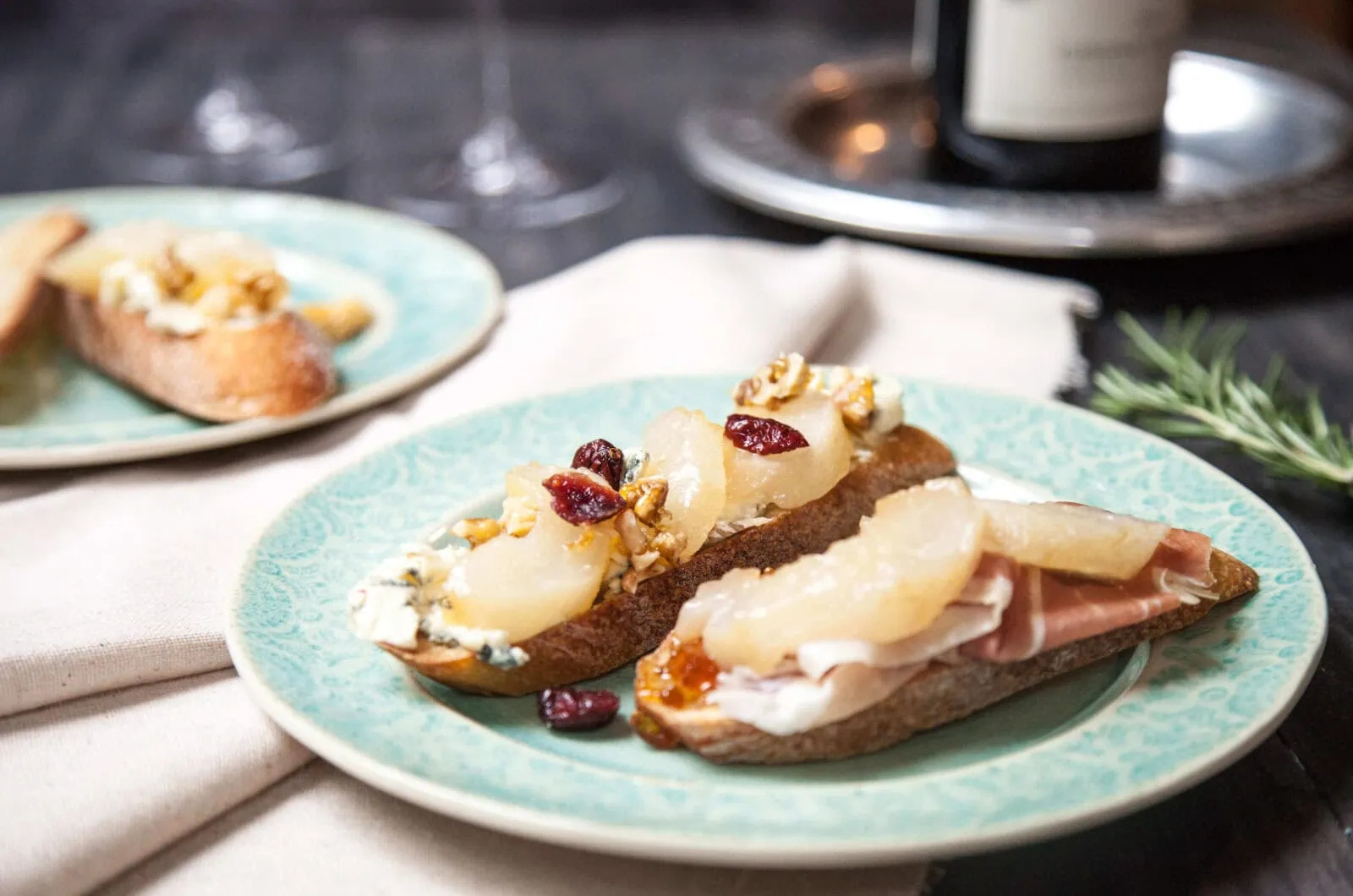 Maple-rosemary roasted pear bruschetta with nuts and dried cranberries on a blue plate.