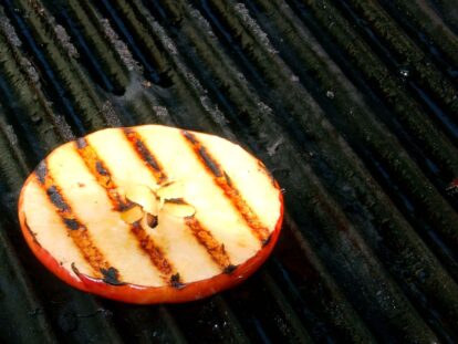 Grilled apple slice with grill marks on a dark grill surface.