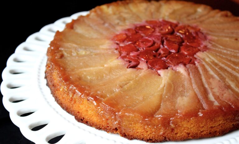 Apple and cherry upside-down cake with caramelized fruit topping on a white plate.