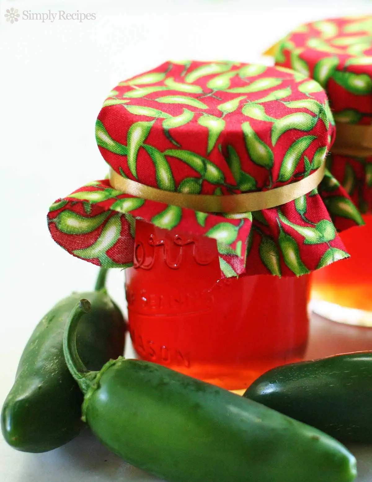 Jalapeno apple pepper jelly jar with jalapenos around it, vibrant and fresh.