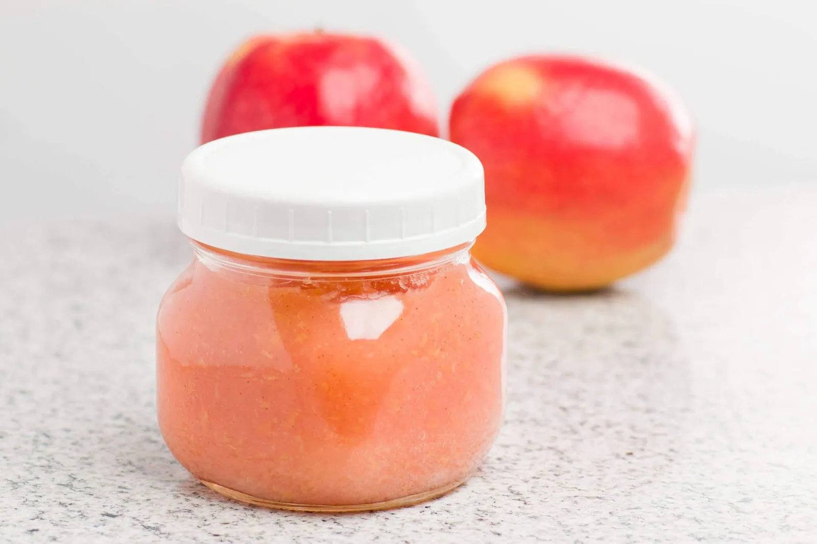 Homemade applesauce in a jar with fresh apples in the background.