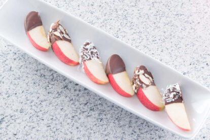 Chocolate-dipped apple slices on a white platter with almond toppings.
