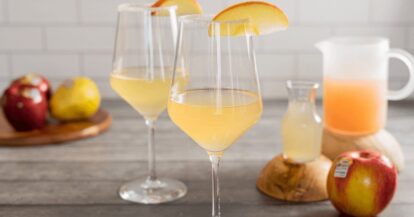 Apple and pear mimosas with fresh fruit on a wooden table.