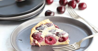 Cherry clafoutis dessert with fresh cherries on a gray plate.
