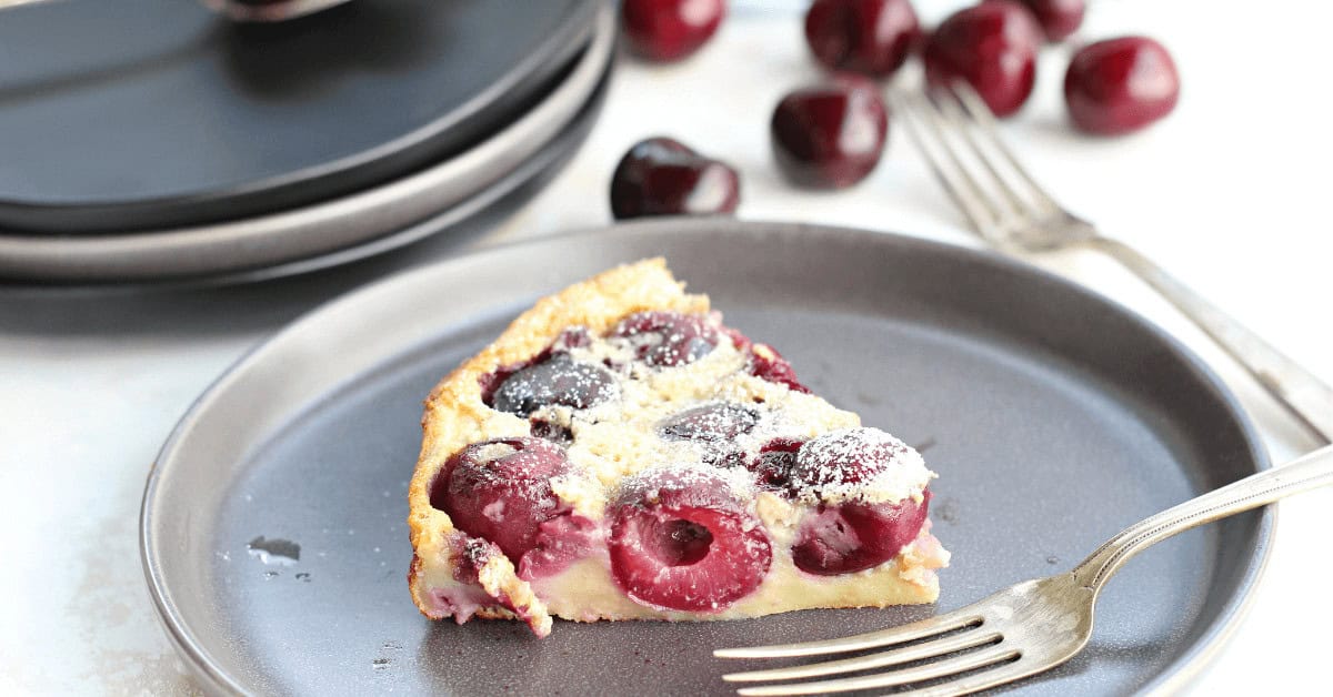 Cherry clafoutis dessert with fresh cherries on a gray plate.