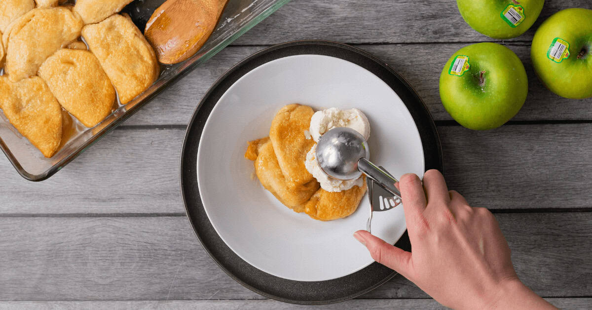 Preparing apple dumplings with a fork on a white plate, green apples nearby.