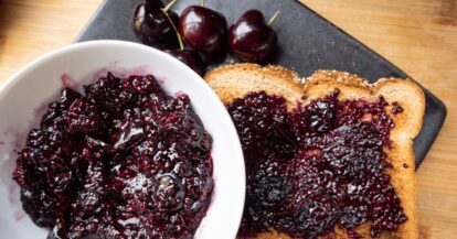 Cherry chia seed jam spread on toast with fresh cherries on a black plate.