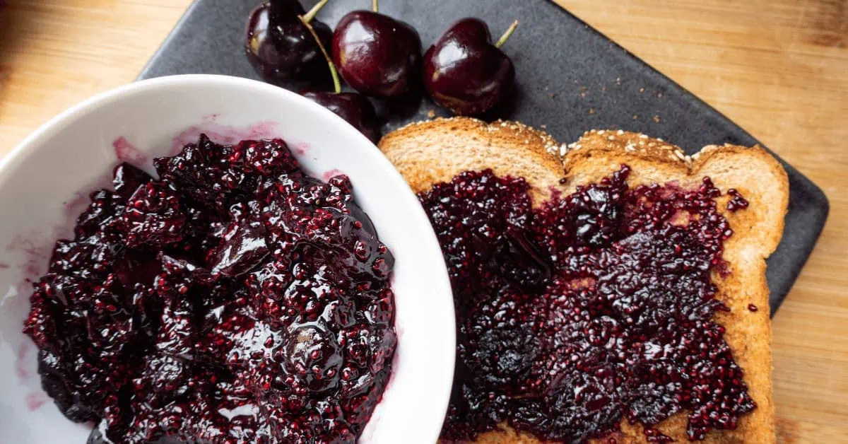 Cherry chia seed jam spread on toast with fresh cherries on a black plate.