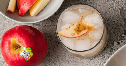 Fresh apple slices in a glass with ice and cinnamon, on a gray surface.