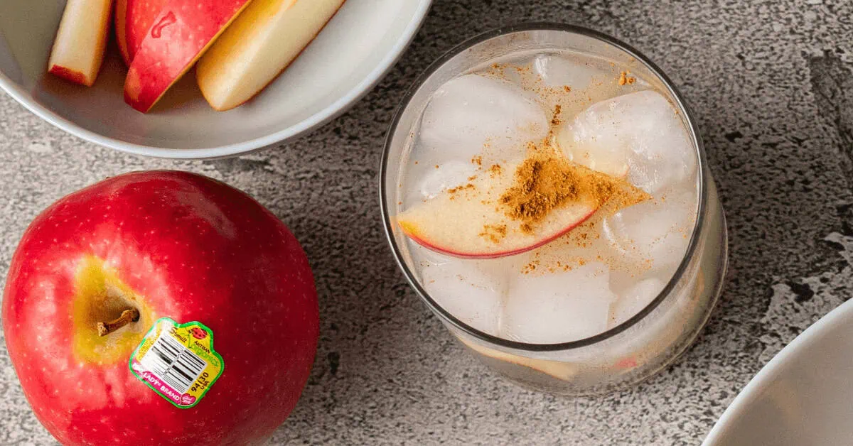 Fresh apple slices in a glass with ice and cinnamon, on a gray surface.