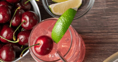 Cherry Limeade cocktail with fresh cherries and lime wedge on wooden table.