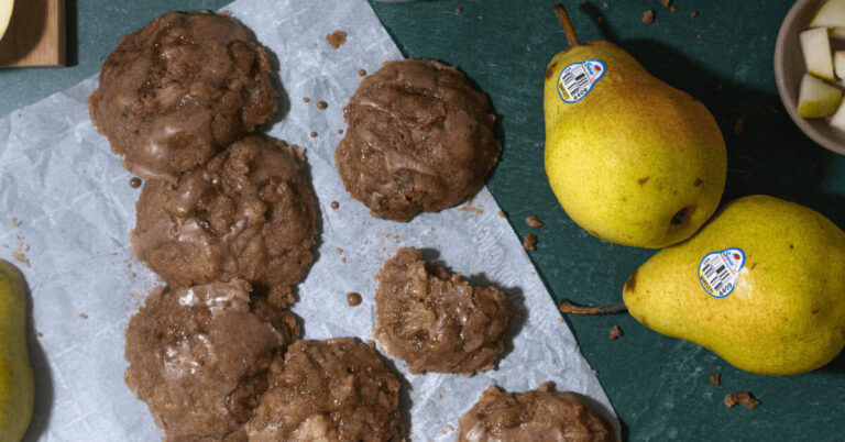 Spiced pear cookies with eggnog drizzle on parchment paper with fresh pears nearby.