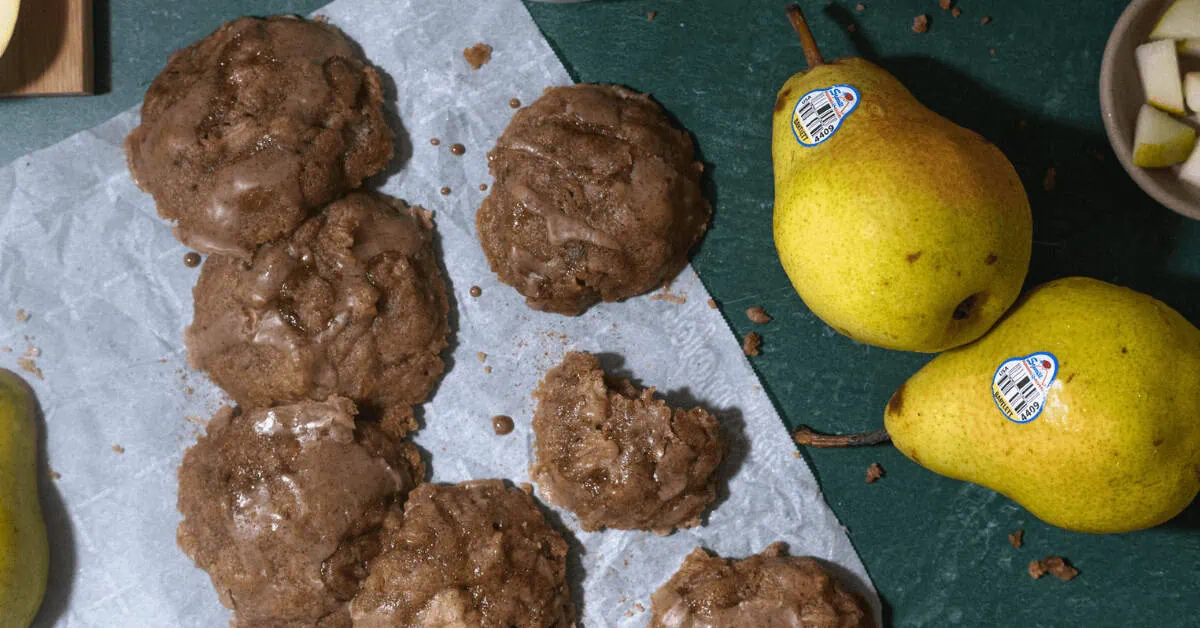 Spiced pear cookies with eggnog drizzle on parchment paper with fresh pears nearby.