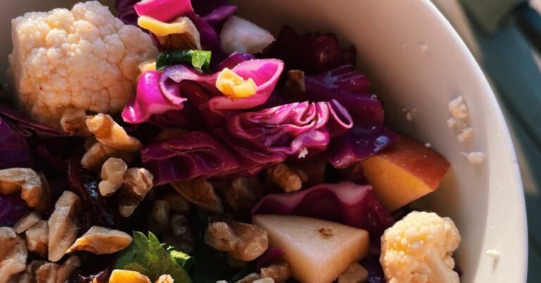 Colorful cabbage, cauliflower, and apple salad with nuts in a bowl.