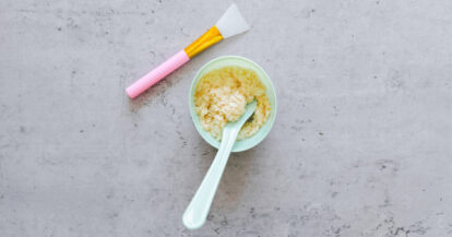 Bowl of apple, oat, and honey face mask with a pink brush on a gray surface.