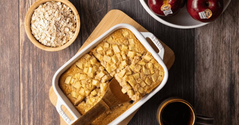 Baked oats with Cosmic Crisp apples in a white casserole dish next to raw oats and a bowl of apples.
