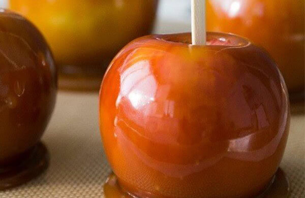 Close-up of a caramel apple with a stick, glossy and golden-brown in color.