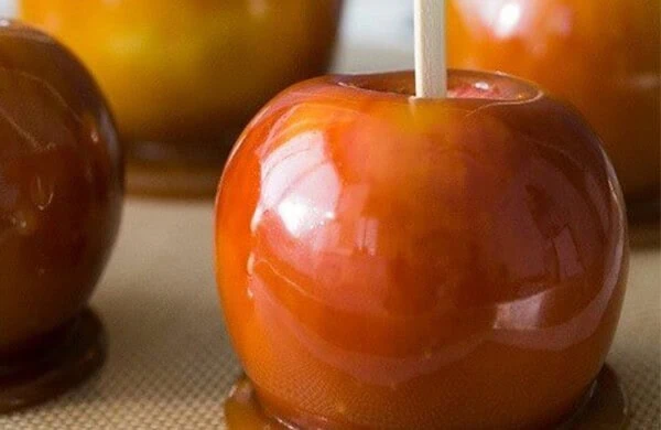 Close-up of a caramel apple with a stick, glossy and golden-brown in color.