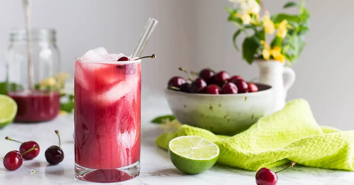 Cherry limeade drink with fresh cherries and lime on a kitchen counter.