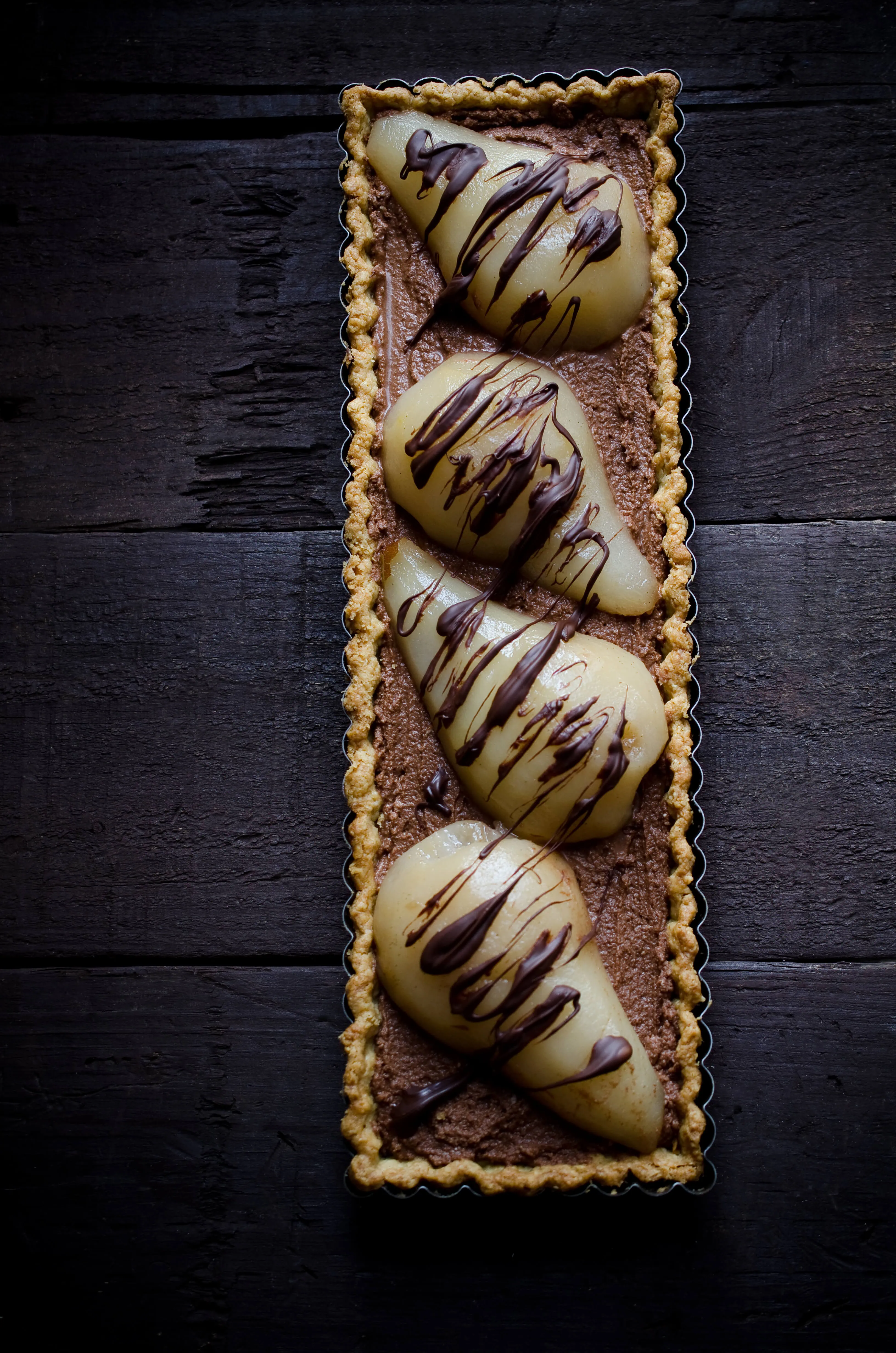 Elegant dessert tart with four pear-shaped chocolates drizzled with chocolate on a dark wooden table.