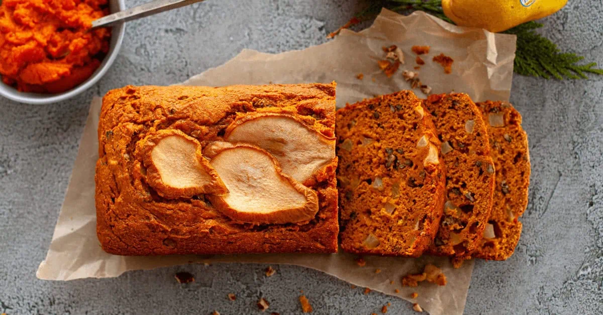 Pumpkin pear bread with sliced pieces on parchment paper, fresh pears in background.