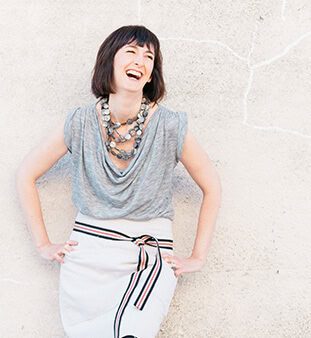 Woman laughing outdoors against a light wall, casual style, joyful mood.