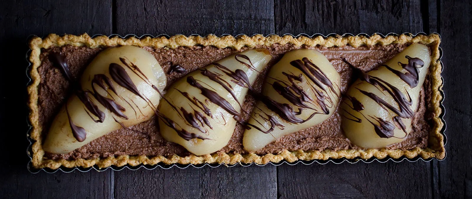 Chocolate mousse tart with poached pears and chocolate drizzle on a dark surface.
