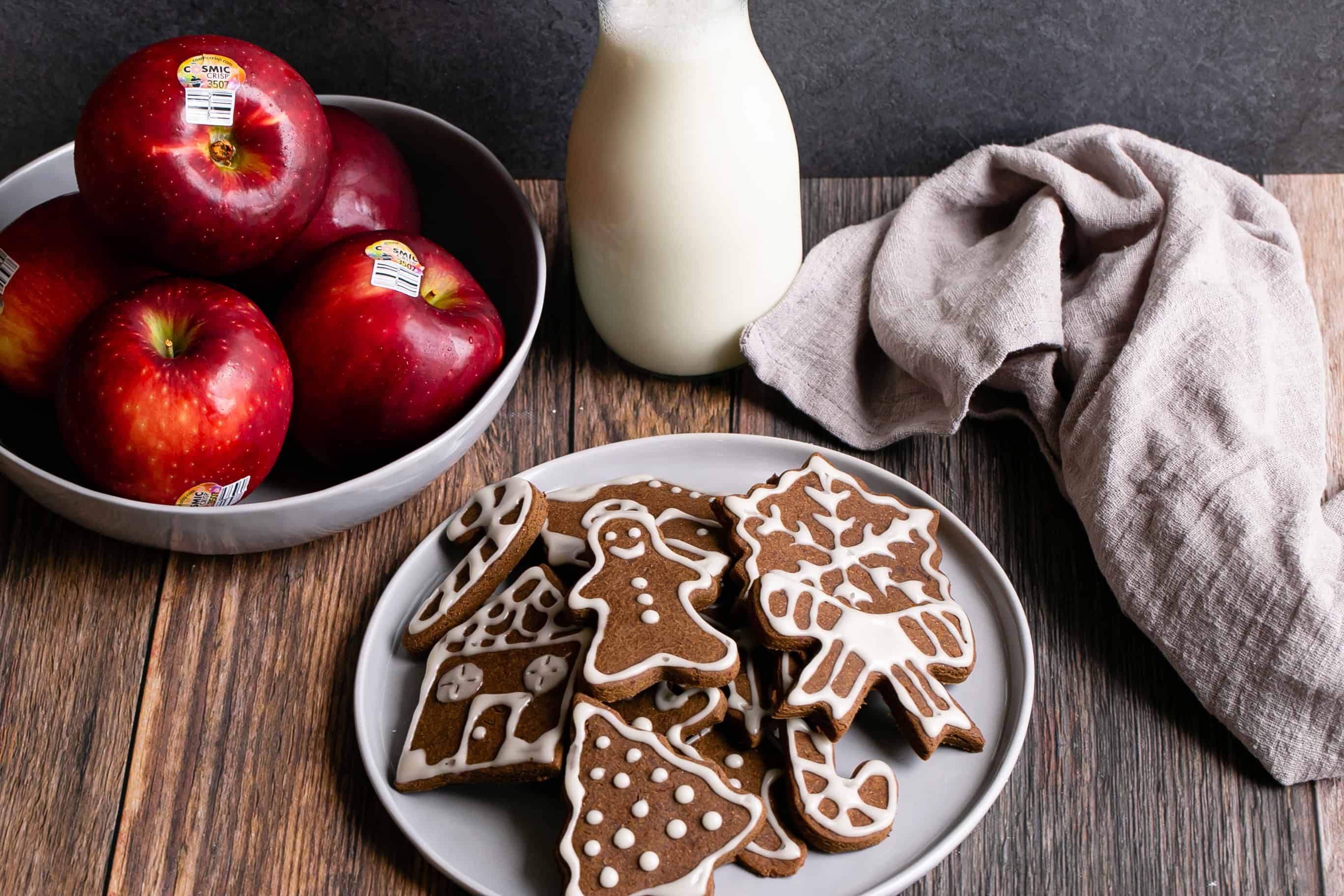 Fresh apples, gingerbread cookies, and milk on a wooden table for holiday treats.