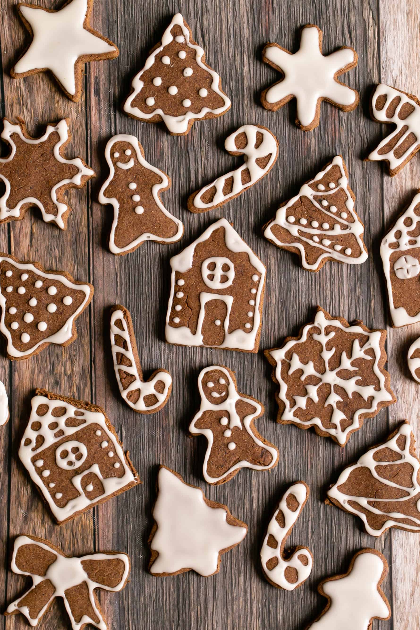 Assorted gingerbread cookies shaped like houses, trees, and holiday figures on wood.