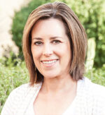Smiling woman outdoors with green foliage in the background.