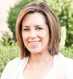 Smiling woman outdoors with green foliage in the background.
