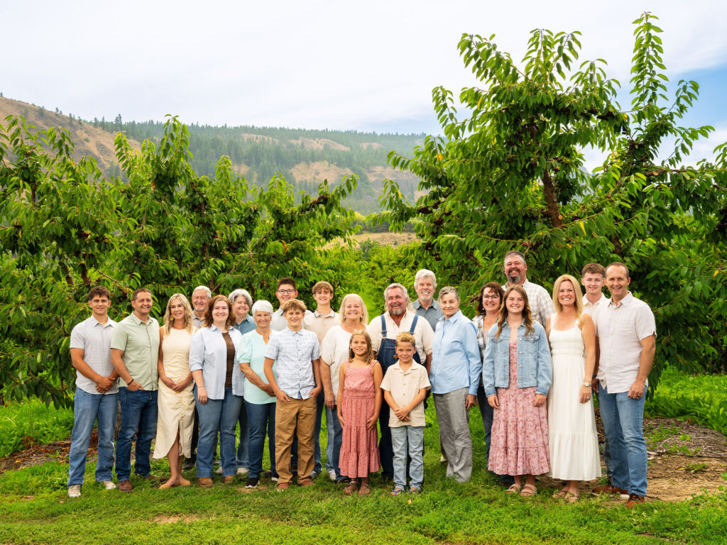 Group of people standing in an orchard with green trees and hills in the background.