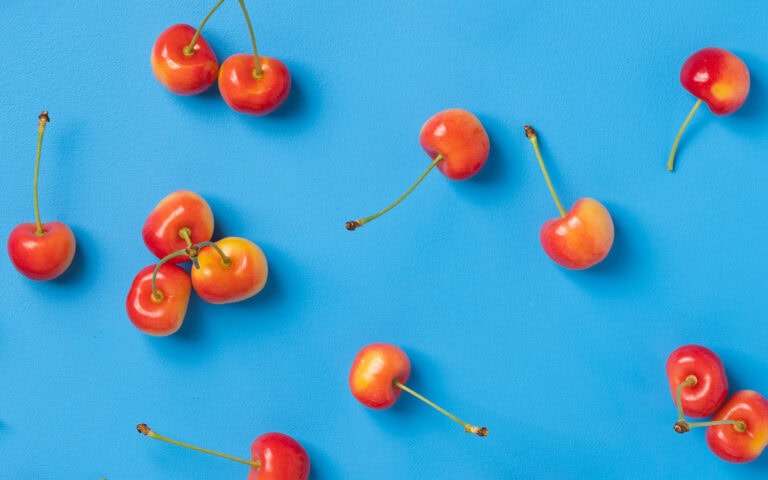 Fresh Rainier cherries scattered on a bright blue background for vibrant visual appeal.