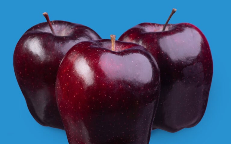 Three shiny dark red apples on a blue background.