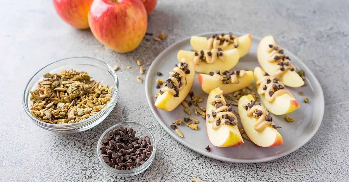 Sliced apple boats topped with chocolate chips and granola on a gray plate.