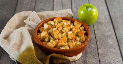 Croutons in a rustic bowl with a green Granny Smith apple on a wooden table.