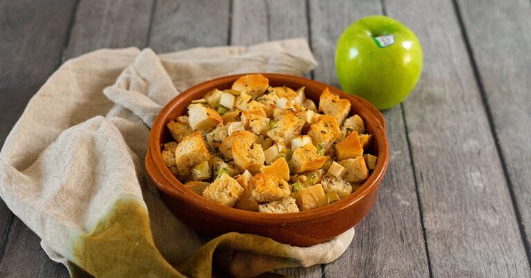 Croutons in a rustic bowl with a green Granny Smith apple on a wooden table.